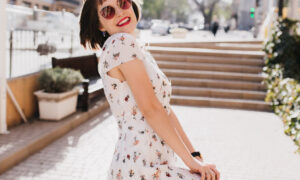 Laughing joyful woman in trendy sunglasses having fun in sunny summer day. Outdoor portrait of pleasant girl with short haircut wears white dress in warm spring morning.